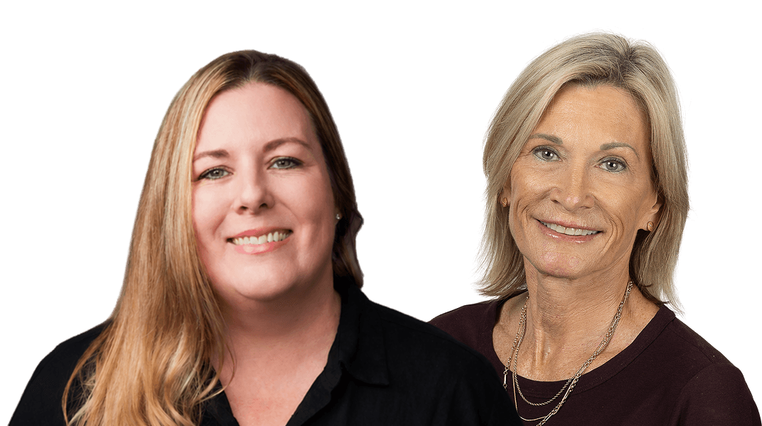 Two smiling older women with silver hair in vibrant blazers.